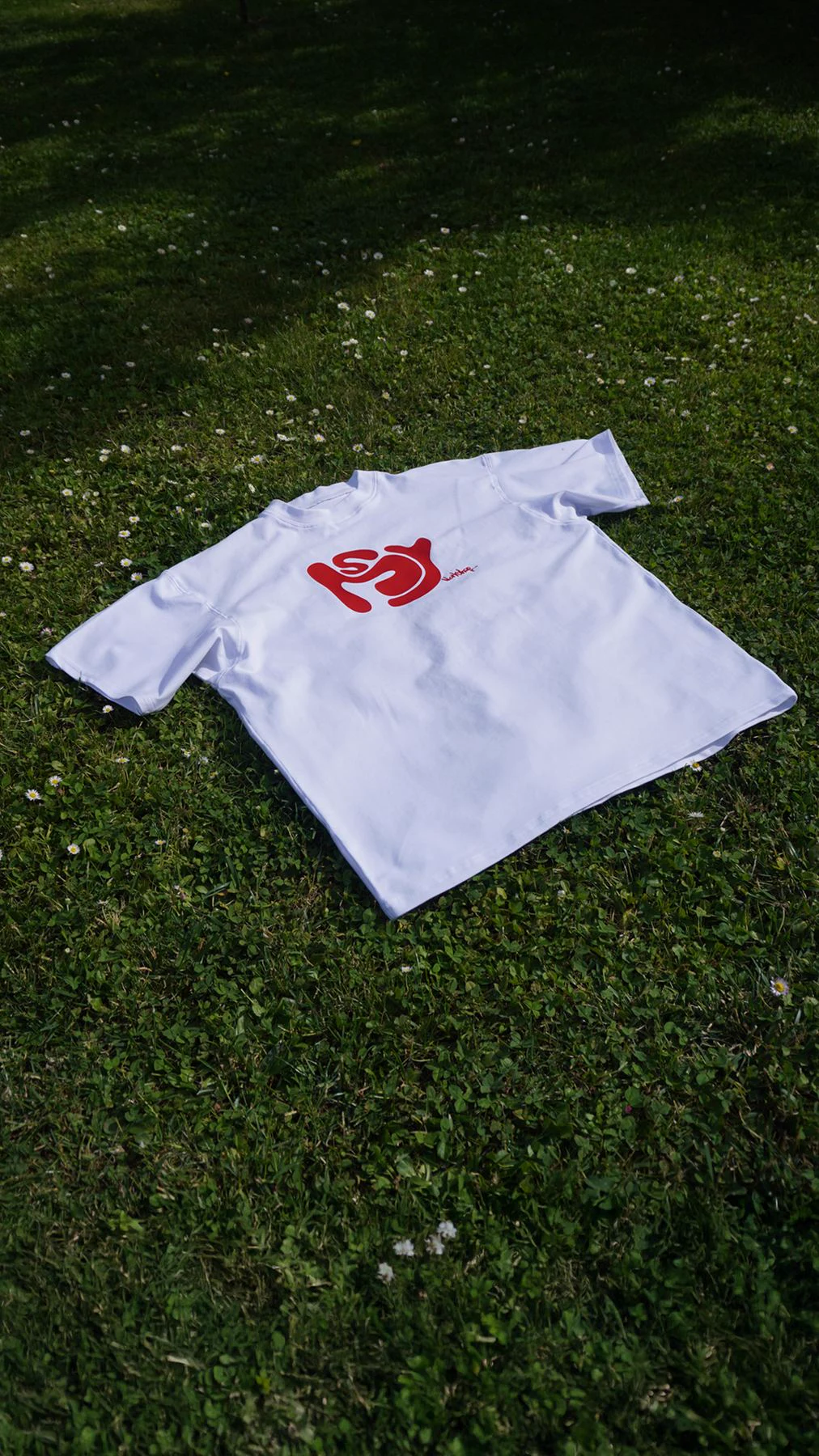T-shirt MSY blanc, logo rouge - packshot produit dans l'herbe